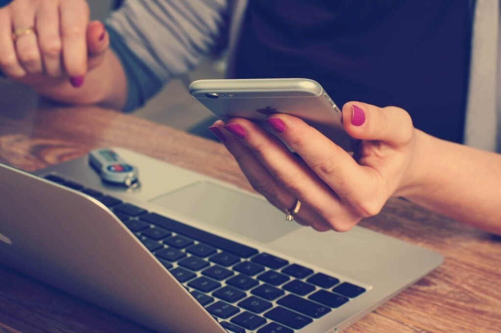 Person looking at phone whilst sat at laptop