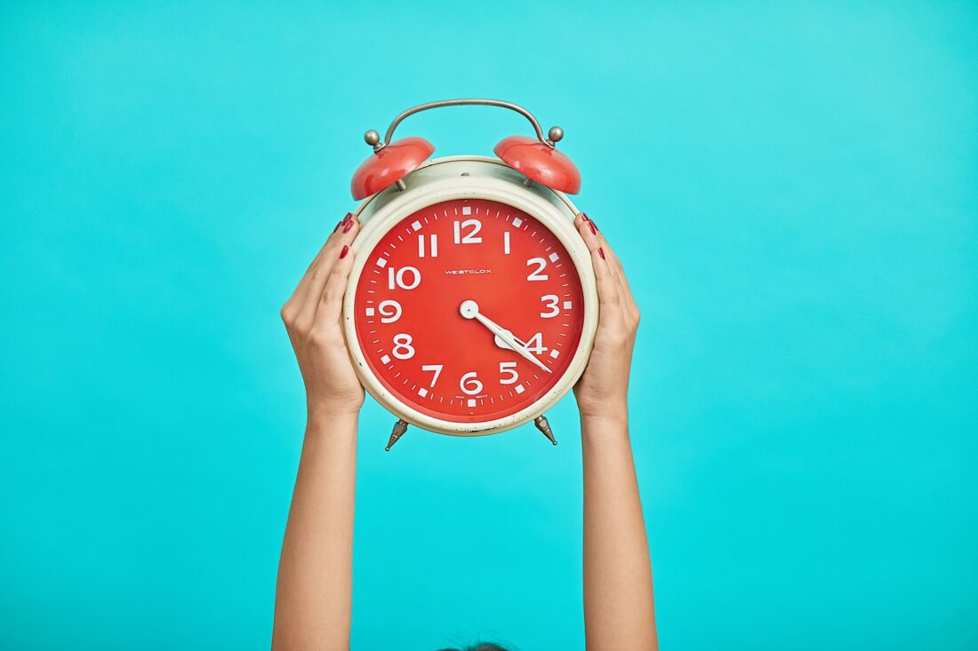 Person holding a large red alarm clock