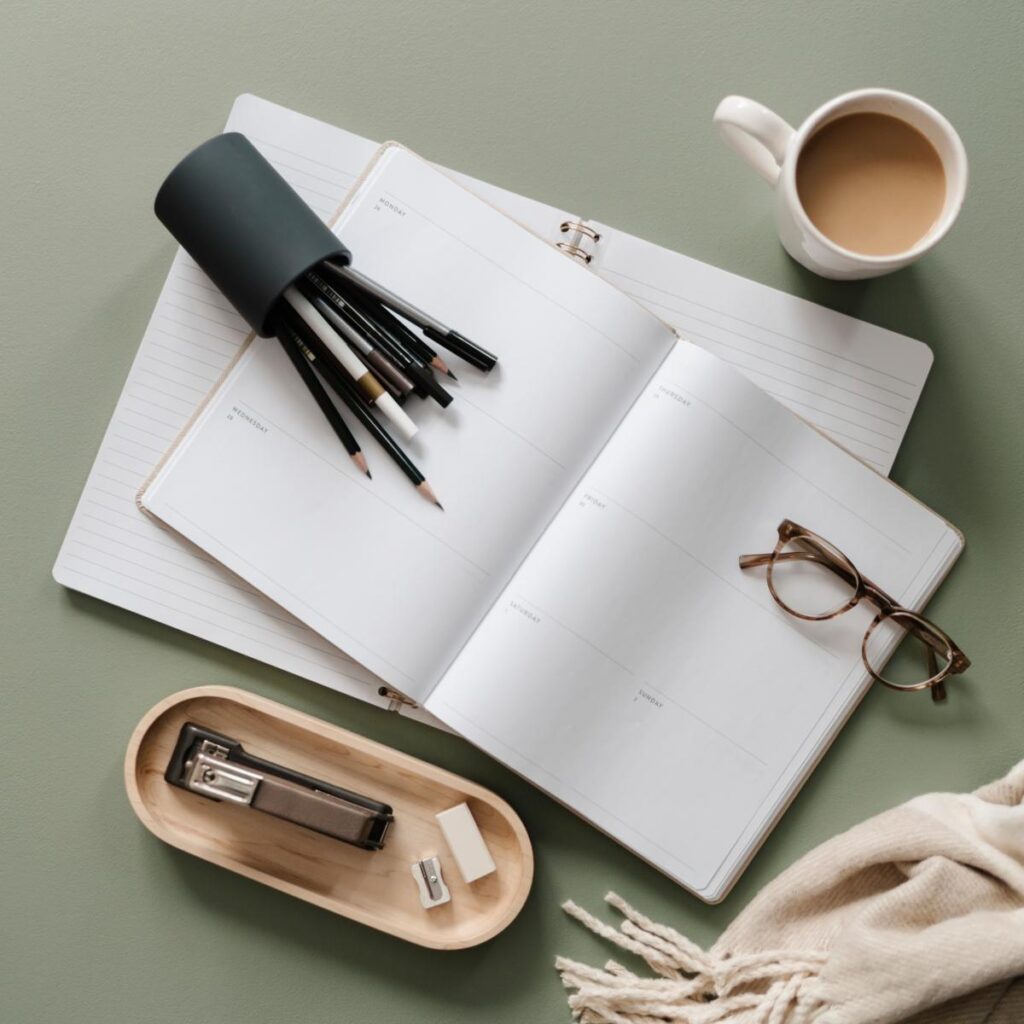 Journal on desk with pencils, hot drink and reading glasses