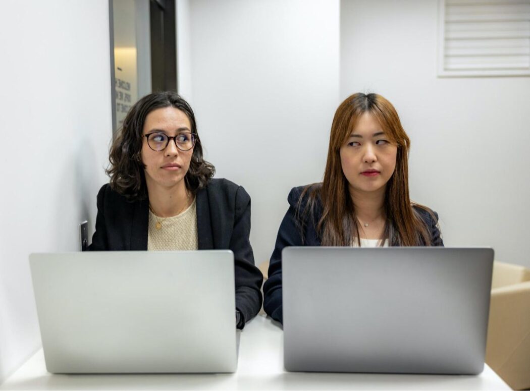 Two people sitting behind laptops in an office looking unsure of one another