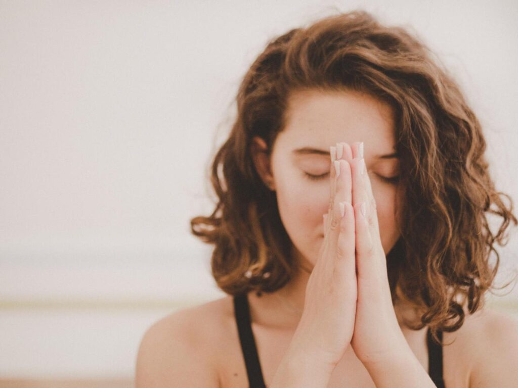 Person giving thanks, with palms placed together in front of their closed eyes